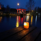 Kerze am Steg vor dem dunklen Eisweiher mit erleuchtetem Pavillon (Weihnachten 2023)
