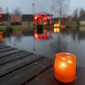 Eisweiher mit einer Kerze am Steg und verschwommenem erleuchtetem Pavillon im Hintergrund (Weihnachten 2023)